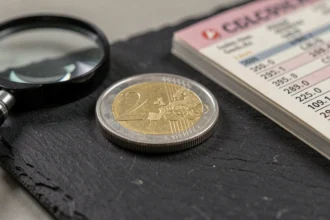 Gros plan d'une pièce de 2 euros Jeux Olympiques posée sur une ardoise avec loupe et guide de cotation numismatique